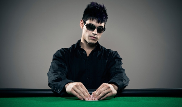 Брюнет в затемненных очках с картами в руках за минуту до совершения хода в покере