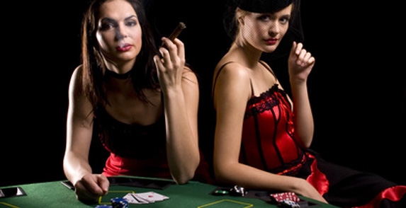 Красотки в эротических красных платьях раскуривают сигару перед игрой в карты
