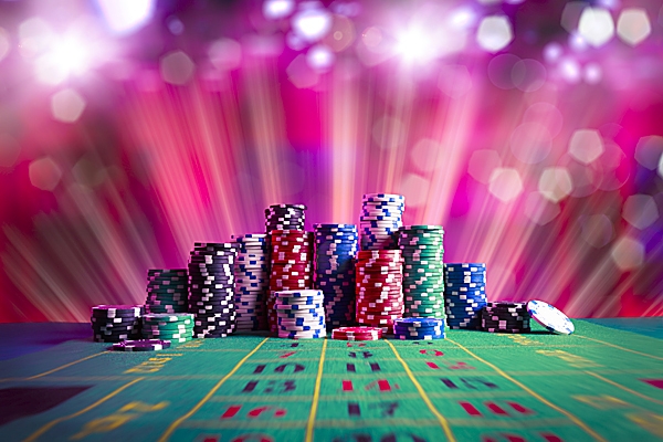 Высокие стопки фишек на игорном столе на фоне розового света