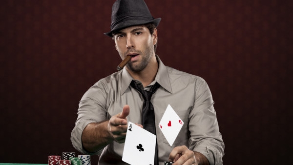 Игрок в покер сидит за игорным столом в шляпе и с сигарой в руках и бросает карты