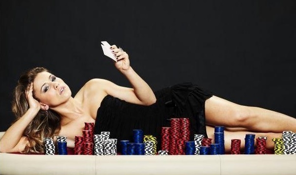 Девушка в черном мини-платье лежит на покерном столе рядом с фишками и держит в руках игральные карты