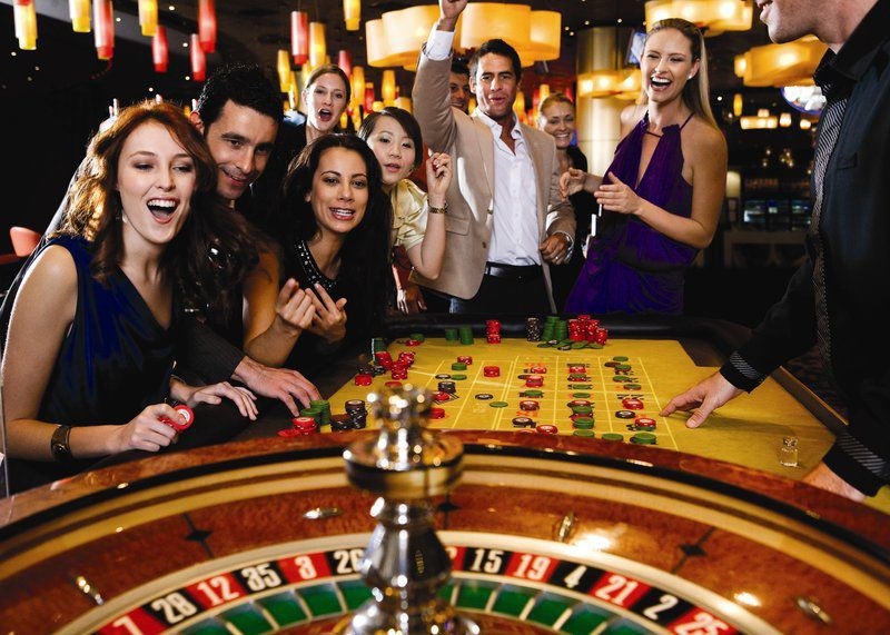 Веселая компания молодых красиво одетых людей болеет за ставки в рулетке