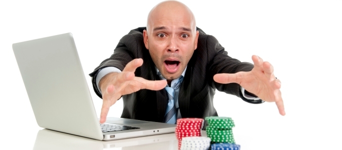 Мужчина в строгом костюме тянется к стопкам фишек, отталкивая свой ноутбук