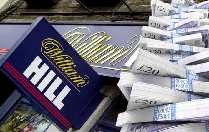Вывеска букмекерской конторы William Hill и стопки из фунтов стерлингов