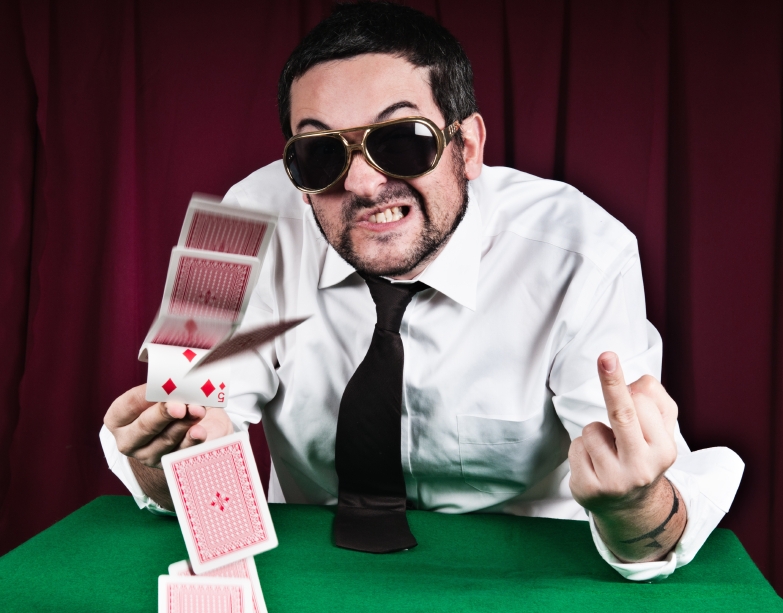 Сердитый мужчина за игорным столом разбрасывает карты и показывает fuck