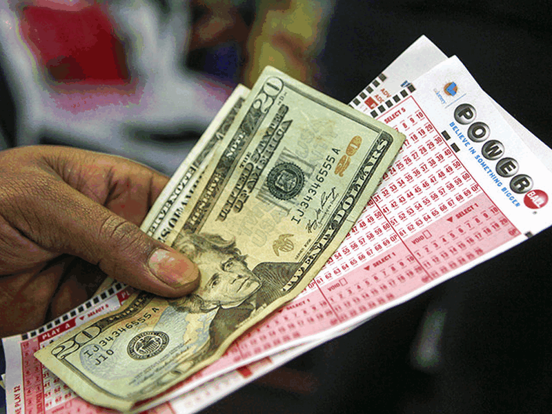 В руке билет PowerBall и долларовые купюры