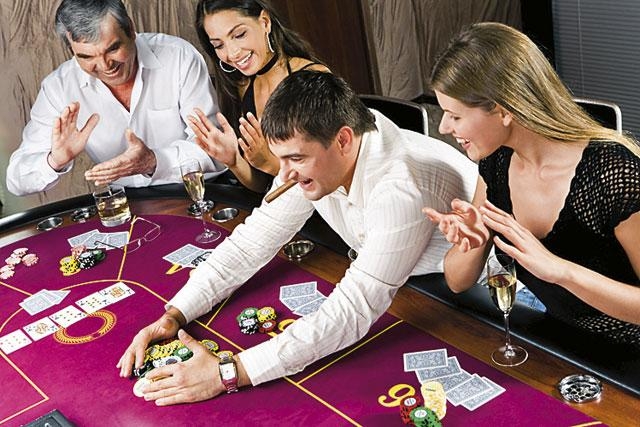 Мужчина с сигарой в зубах сгребает выигранные фишки в присутствии двух женщин и противника