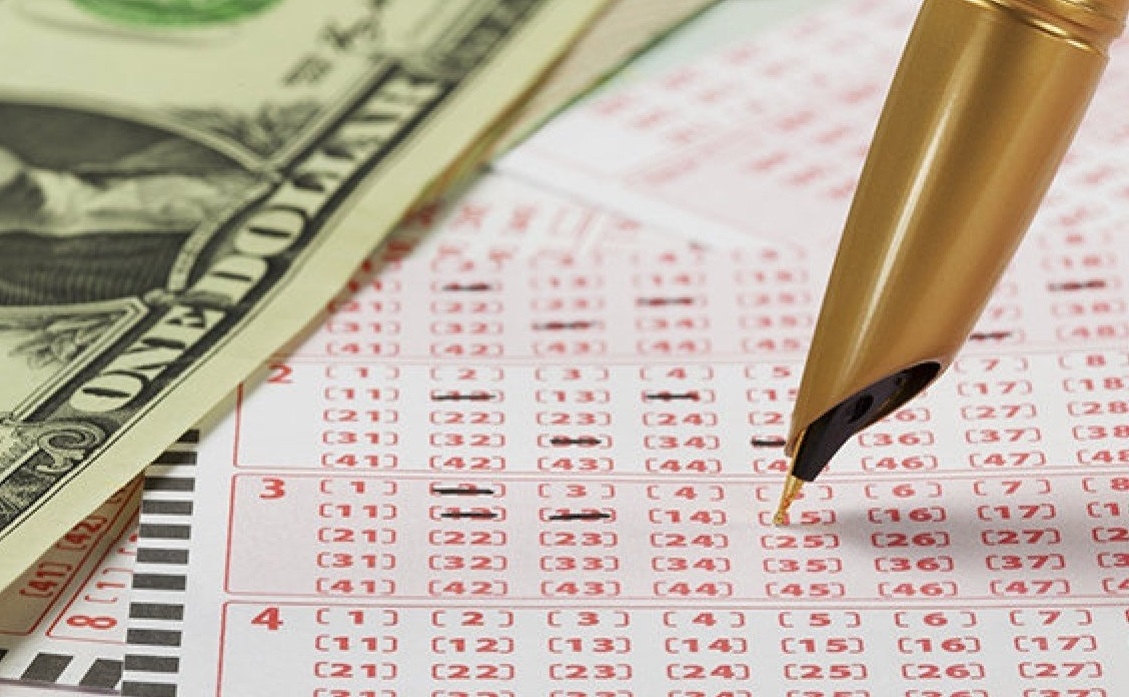 Ручка, заполняющая лотерейный билет, и стодолларовая купюра