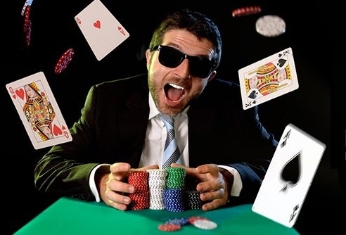 Мужчина затемненных очках и в строгом костюме швыряется картыми и фишками за столом для игры в покер