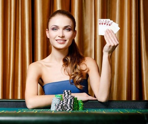 олодая красивая девушка в голубом платье демонстрирует карты червовой масти за игорным столом
