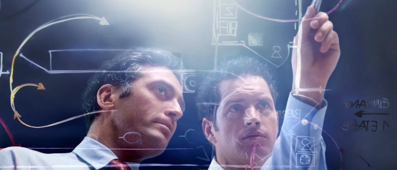 Двое мужчин разбирают схему в офисе на доске