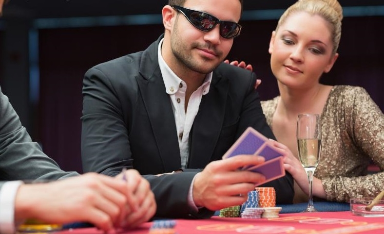 Мужчина в деловом костюме и затемненных очках играет в покер в компании красивой блондинки