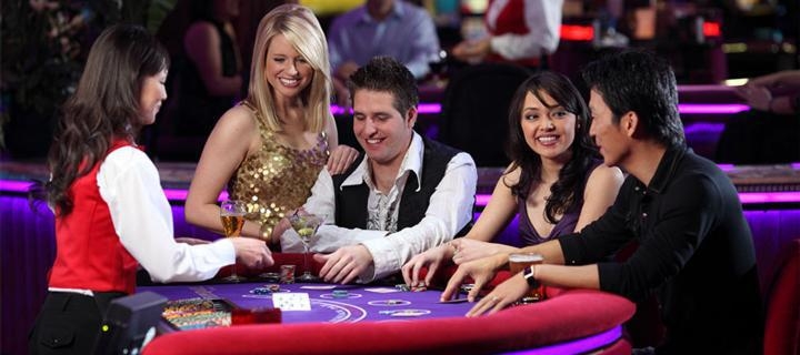 Красивые молодые люди за игрой в Оазис покер в компании девушки-дилера в дорогом престижном казино