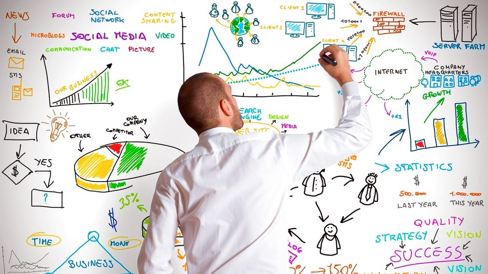 Мужчина в белой рубашке расписывает схемы на доске