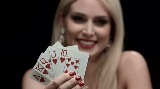 Блондинка игриво улыбается, демонстрируя карты червовой масти