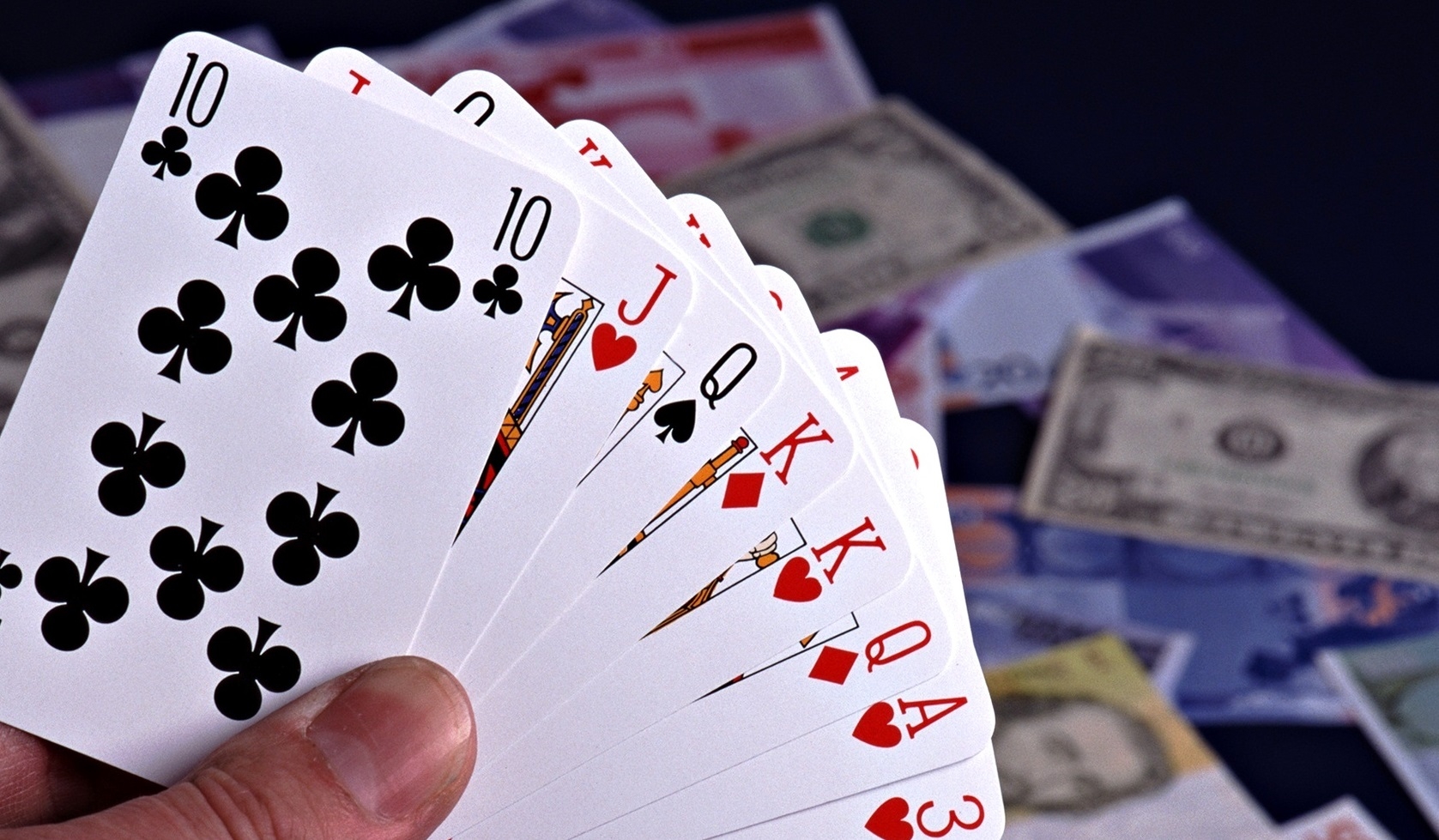 В руке игрока веер из карт, а на заднем фоне деньги разных стран мира