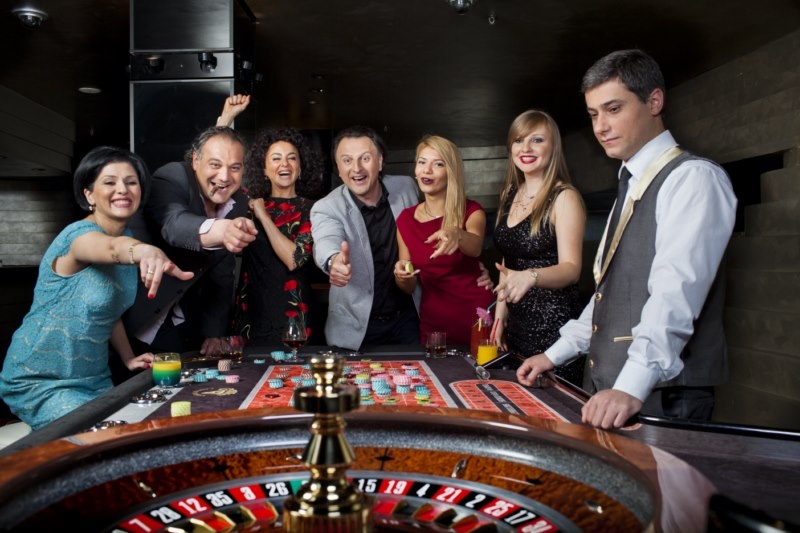 Женщины и мужчины веселятся и распивают коктейли за игрой в рулетку