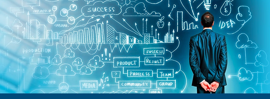 Мужчина в деловом костюме стоит лицом к доске со схемами