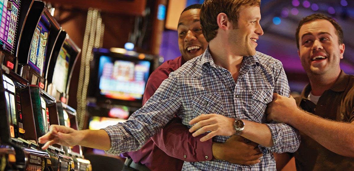 Двое парней оттаскивают от игрового автомата своего азартного друга