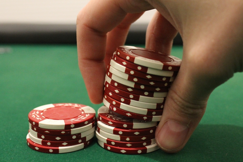 Рука игрока, которая ставит стопку красных фишек на игорный стол