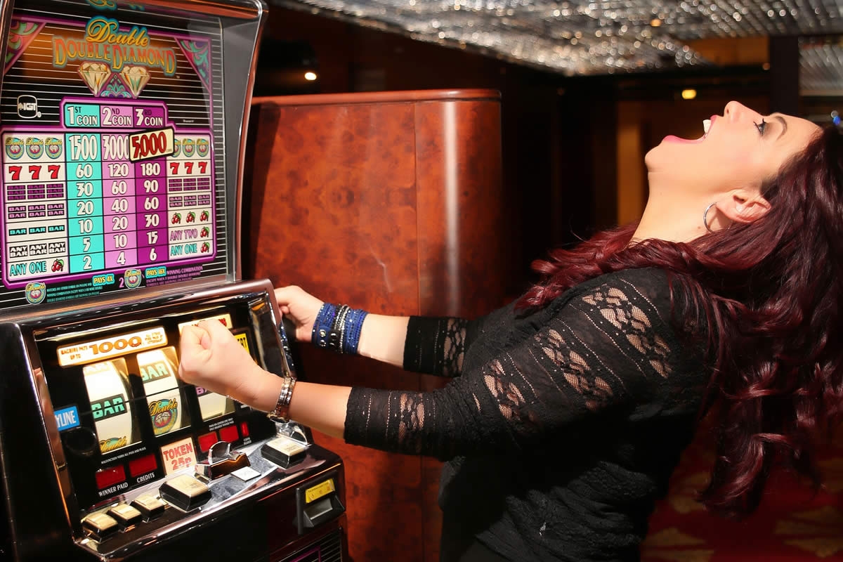 Девушка запрокинула голову и в восторге кричит, сидя за игровым столом