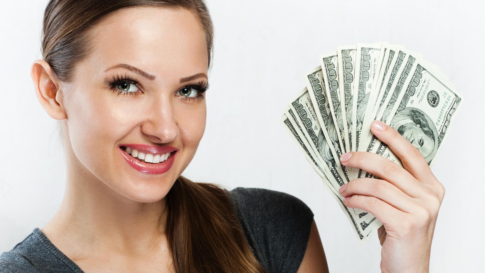 Красивая девушка обворожительно улыбается, держа в руках веер из стодолларовых купюр