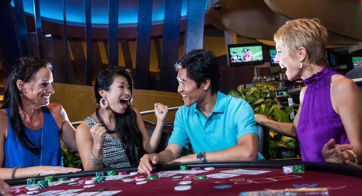 Молодой азиатский парень развлекает троих девушек за игорным столом во время игры в покер