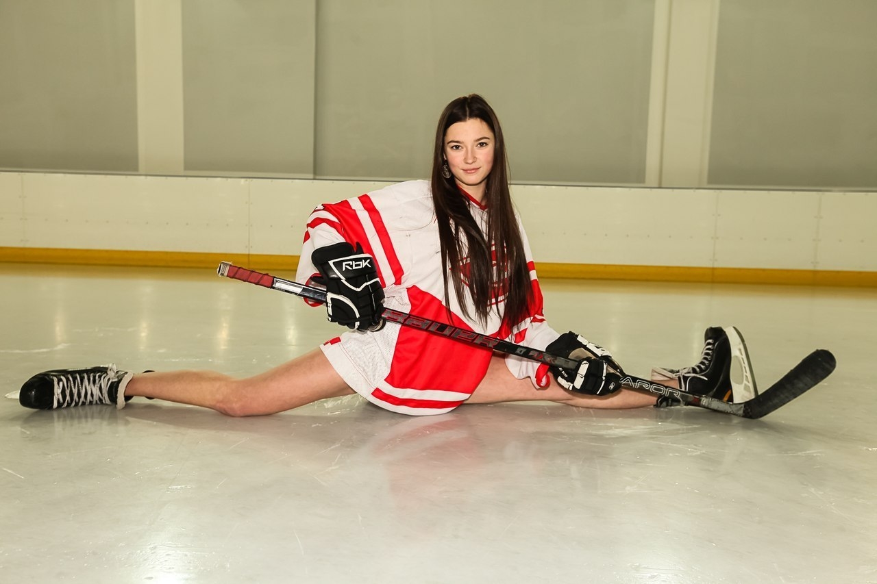 Брюнетка в хоккейной форме с голыми ногами сидит на шпагате на льду