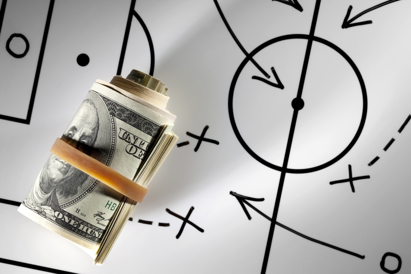 Доллары, перетянутые резинкой лежать на схеме футбольного матча