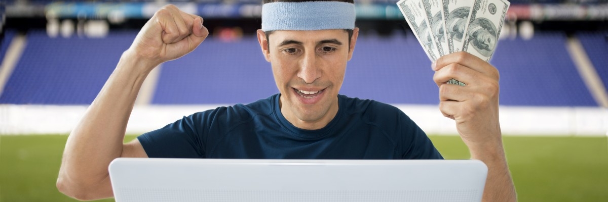 Беттер с долларами в руках болеет за свои ставки перед ноутбуком на футбольном поле