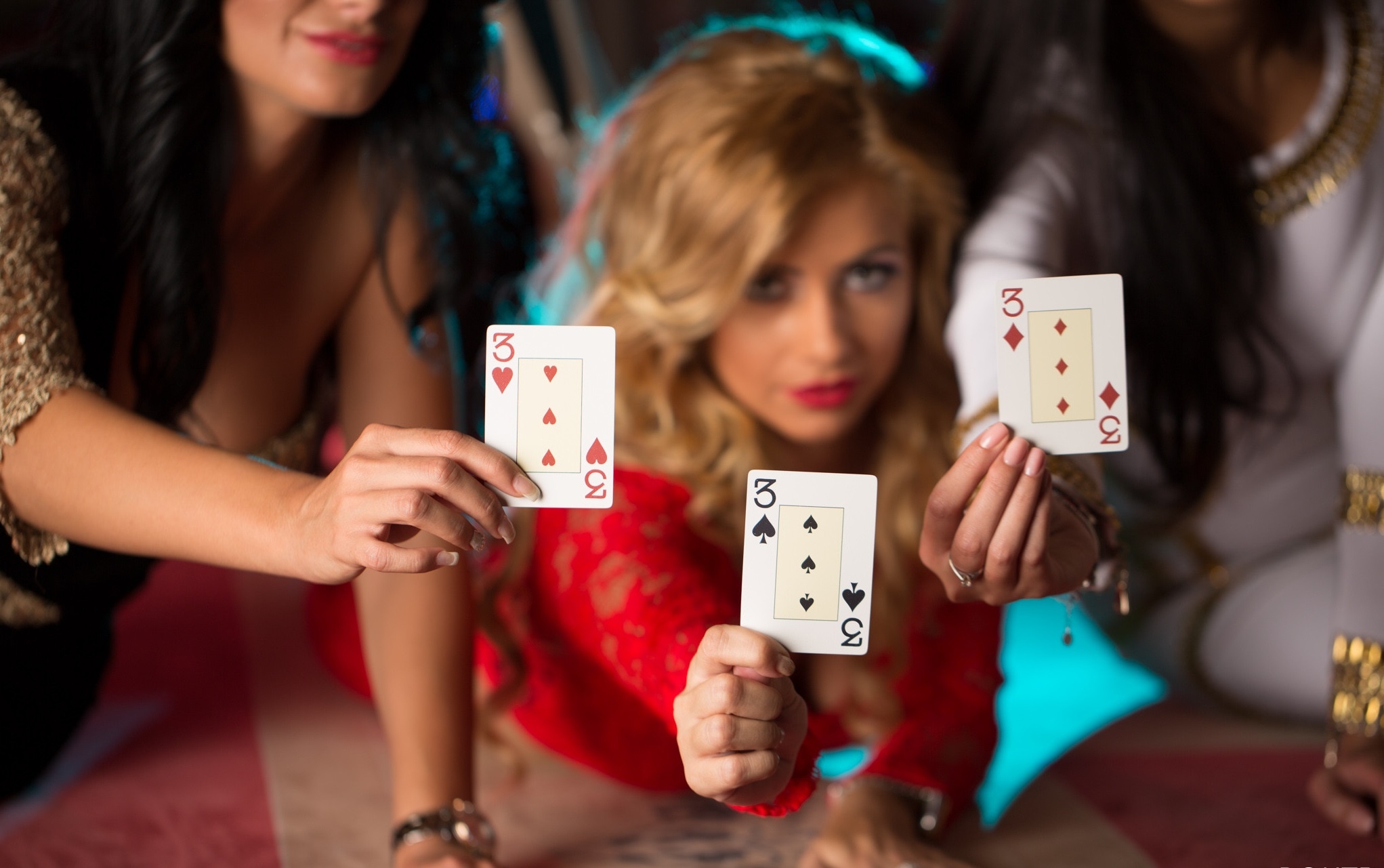 Трое горячих красоток в вечерних платьях демонстрируют карты, сидя на столе для покера
