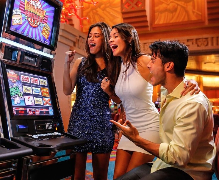 Две стройные подружки в мини-платьях болеют за красавчика, который играет на автомате