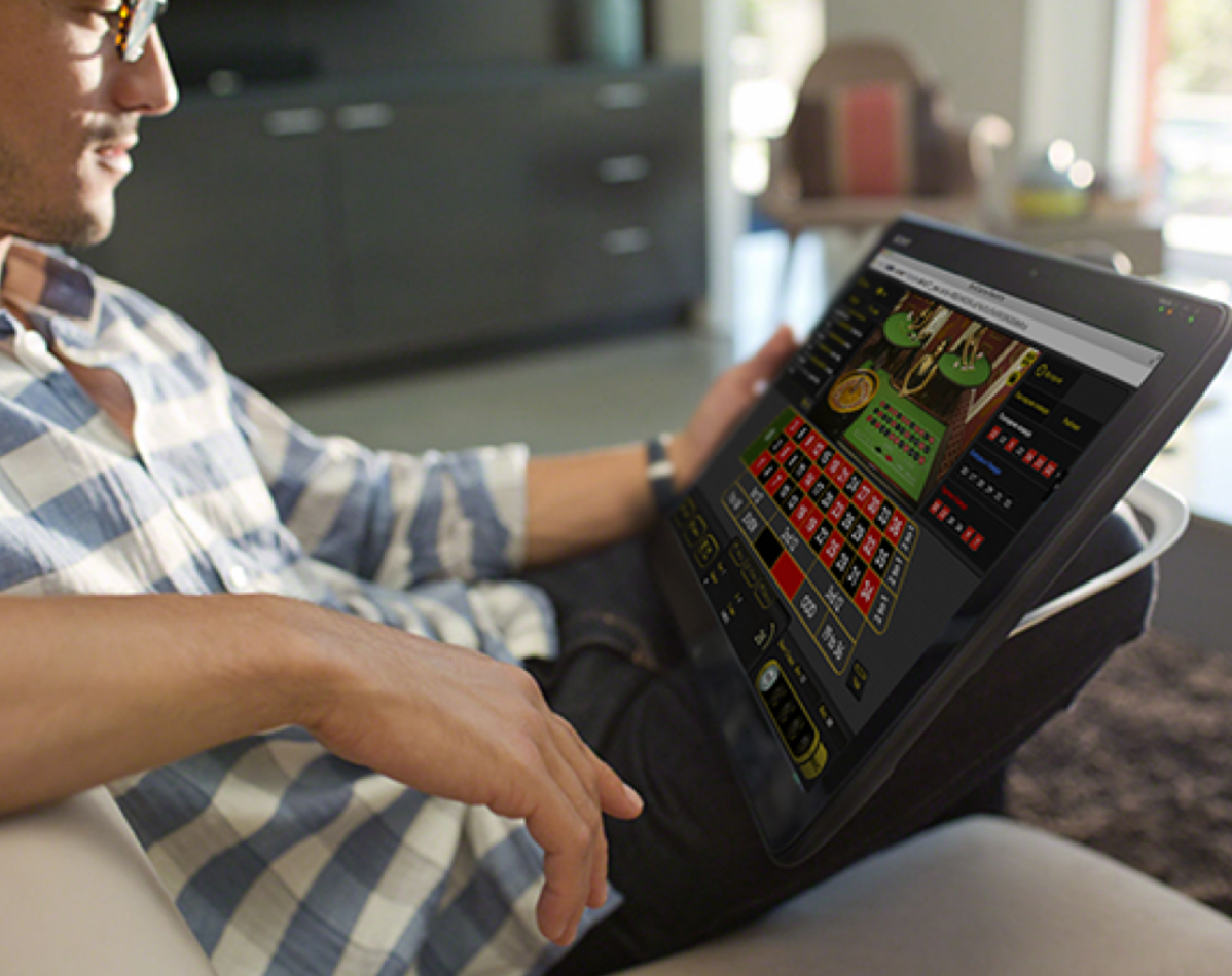 Мужчина играет в онлайн рулетку, удобно умостившись на диване в планшетом в руках