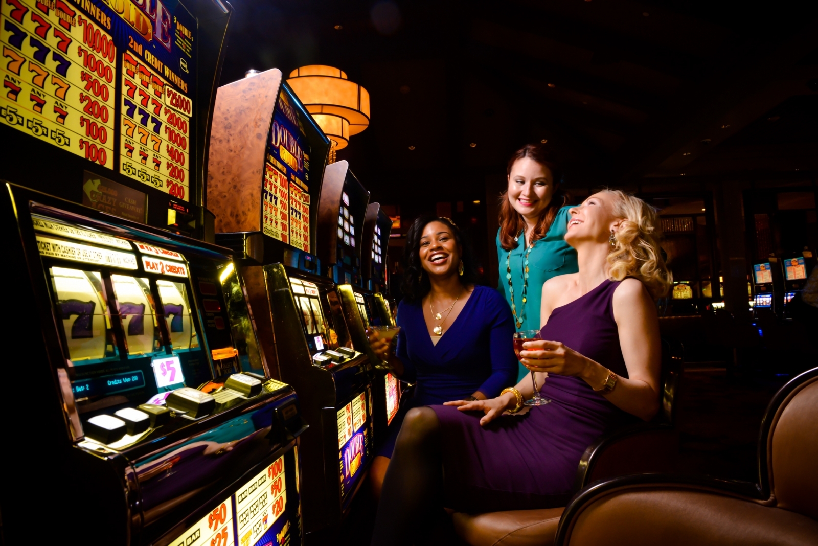 Три подруги в откровенных вечерних платьях веселятся за игрой на слотах в дорогом казино