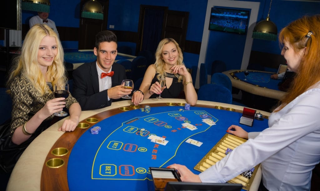 Молодой элегантно одетый мужчина распивает виски за игрой в покер в компании двух сексуальных девушек