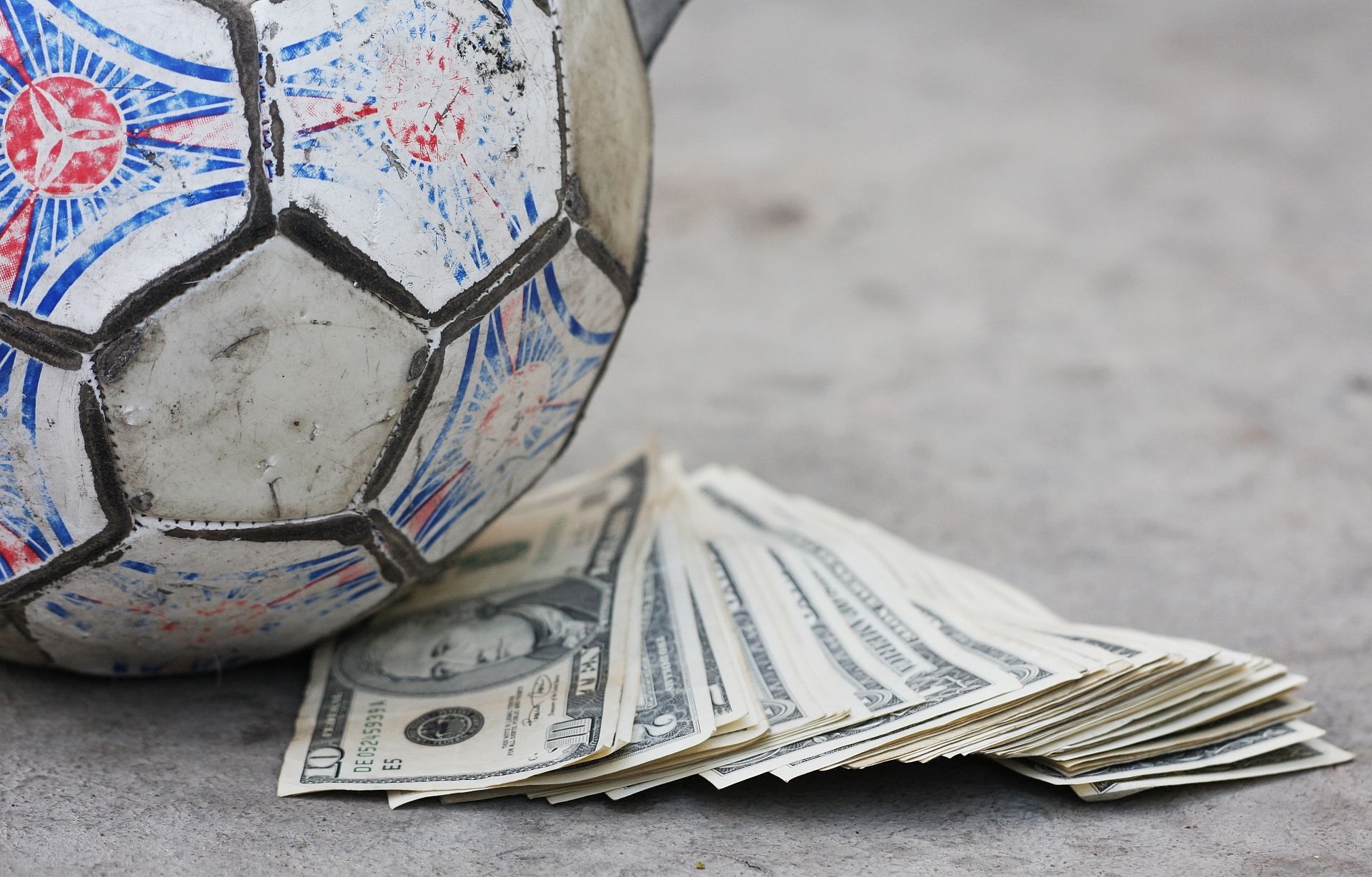 Истрепанный футбольный мяч, рядом с которым рассыпаны долларовые купюры