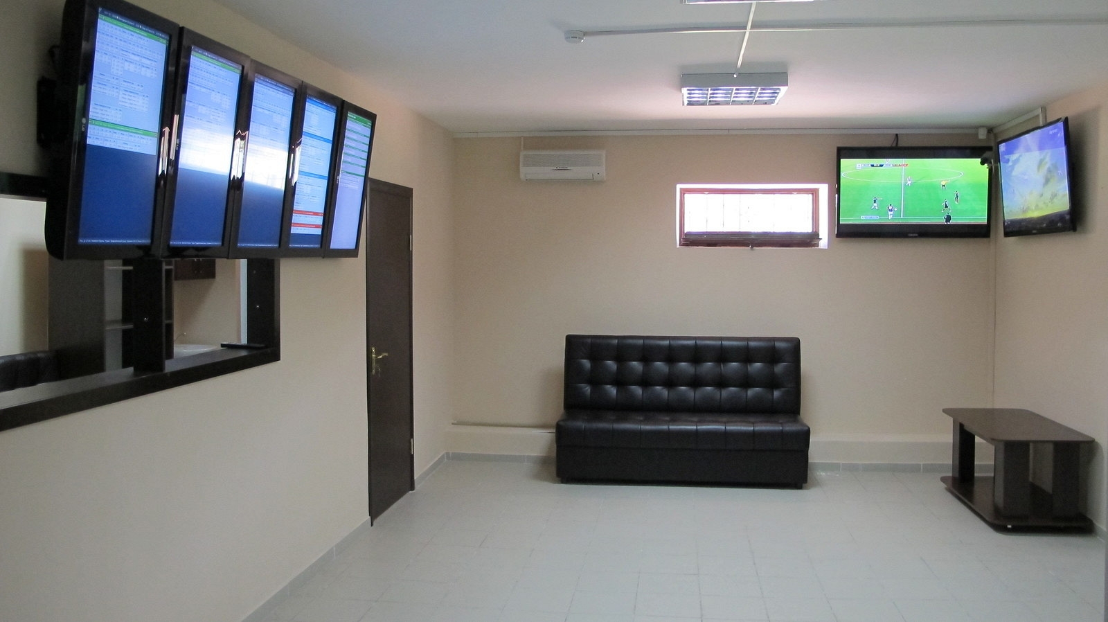 Комната для совершения ставок, в которой стоит черный кожаный диван, а на стенах висят мониторы с коэффициентами
