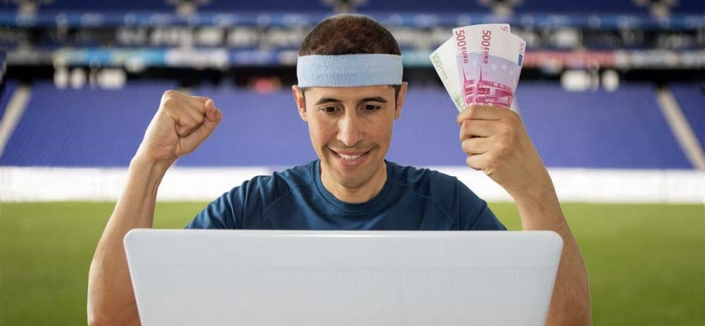 Мужчина совершает ставки на спорт с помощью ноутбука, находясь на футбольном поле