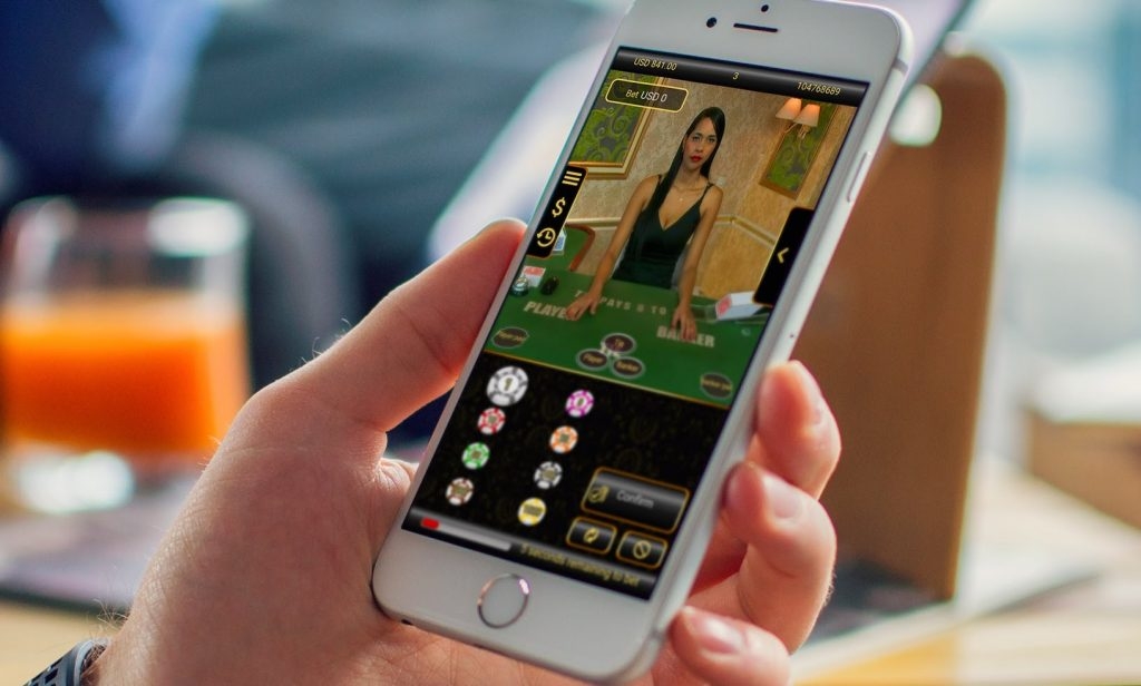 Игрок держит смартфон, на котором идет трансляция азартной игры с настоящим крупье