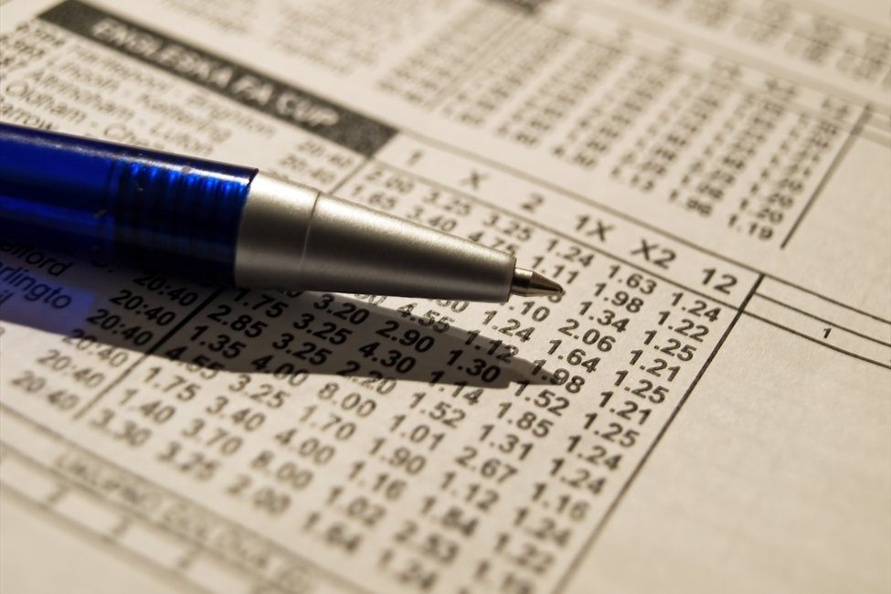 Лист с коэффициентами от букмекерской конторы и шариковая ручка на нем