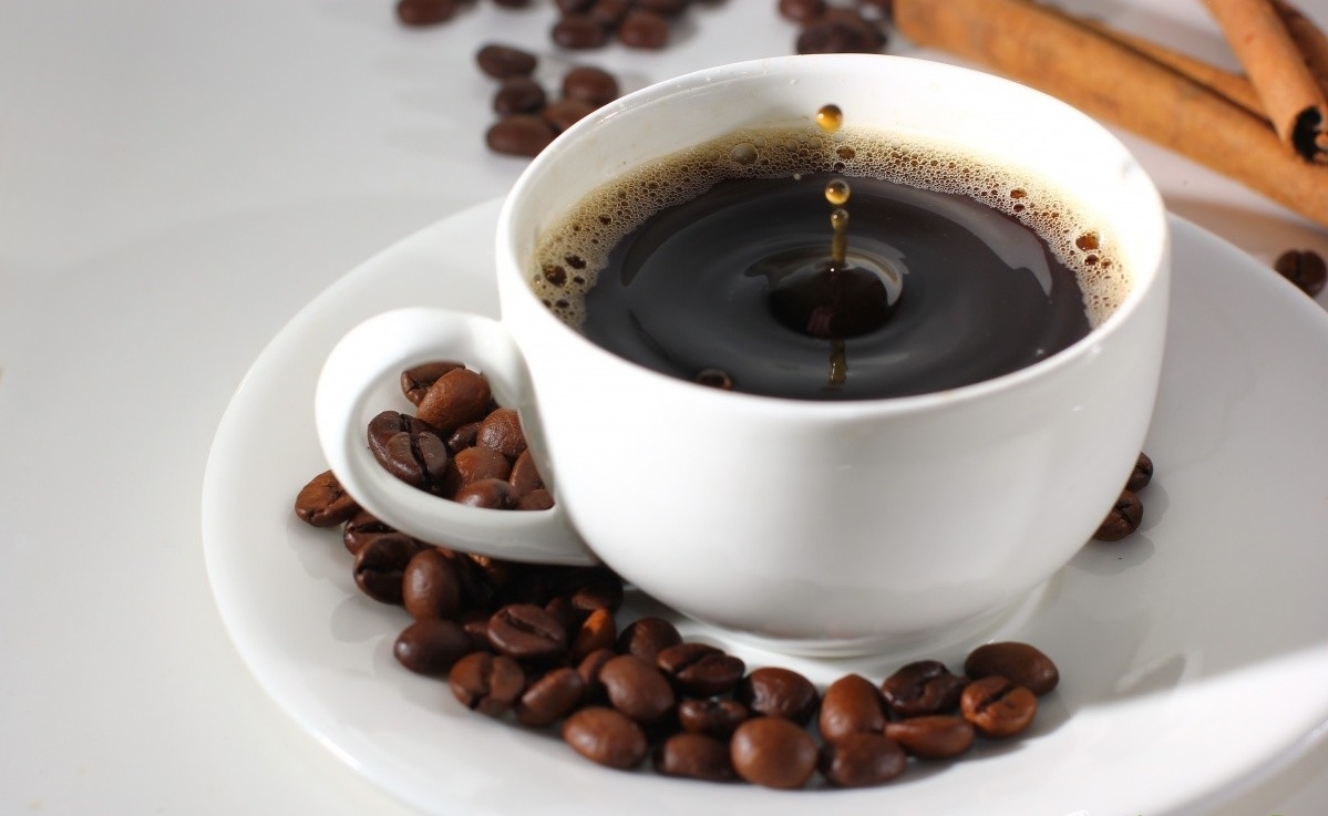 В белой чашке стынет кофе, а рядом на белом блюде лежат зерна кофе