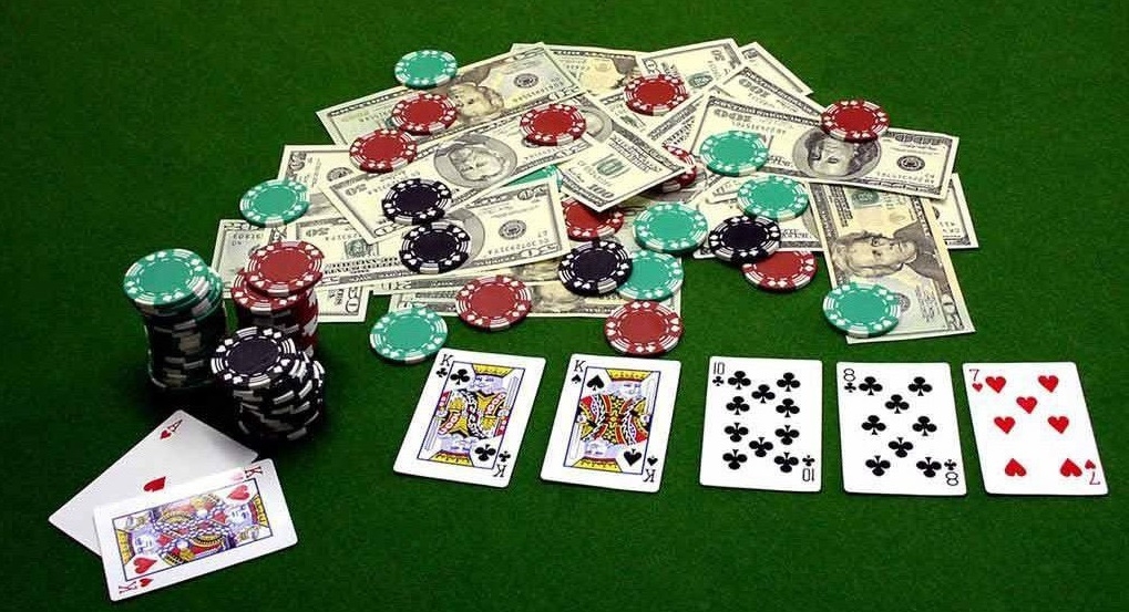 На столе для игры в покер лежит карты, фишки и куча стодолларовых купюр