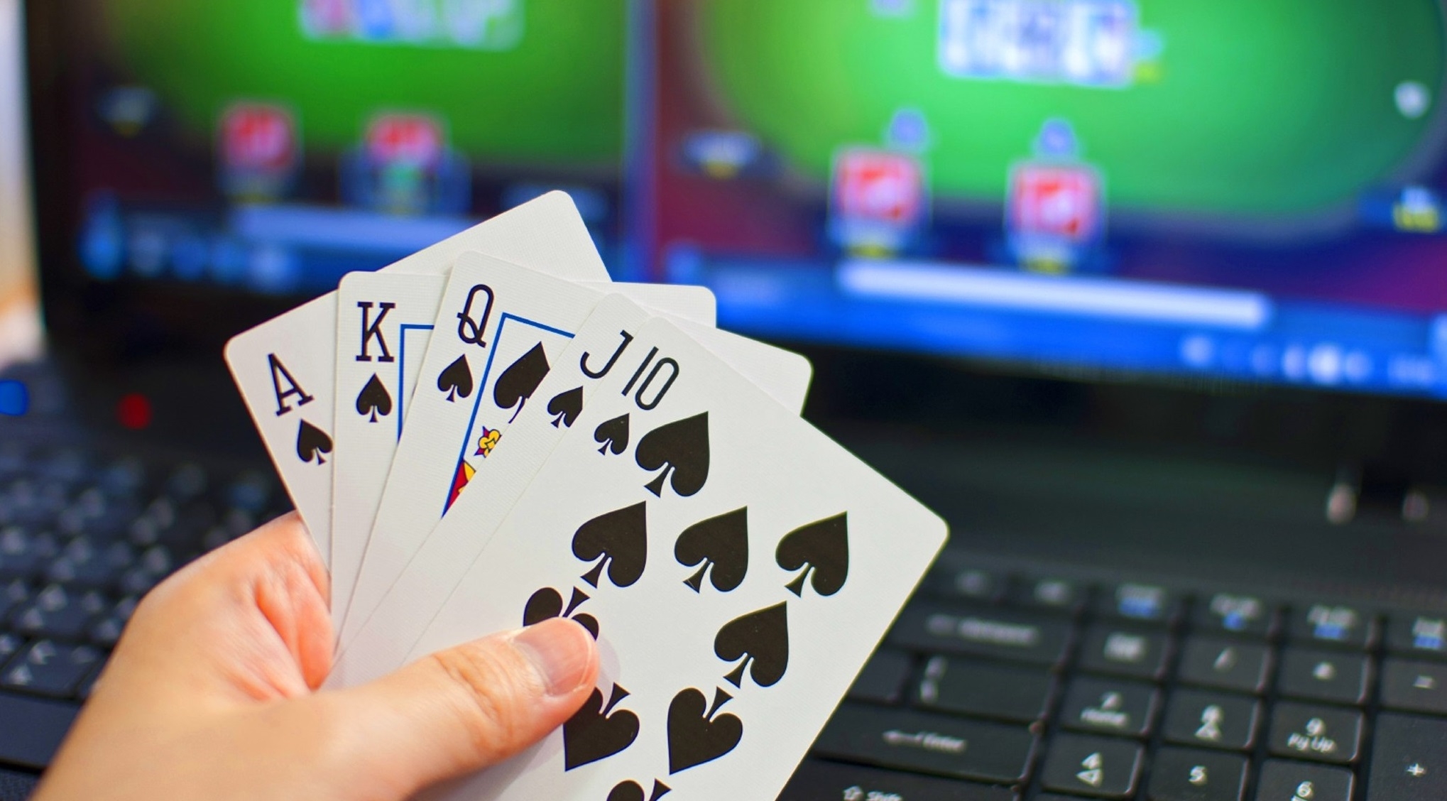 Игрок держит карты пиковой масти, сидя перед монитором ноутбука, на котором открыта игра в покер