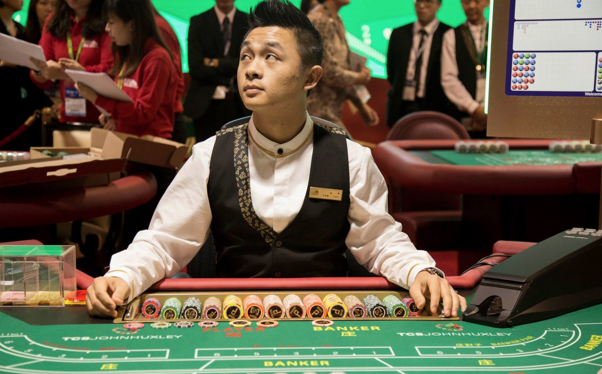 Молодой парень-крупье ждет игроков у слота для баккара