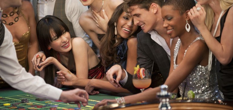 Красивые и эллегантные женщины и мужчины улыбаются, совершая свои ставки за игорным столом в зале престижного казино