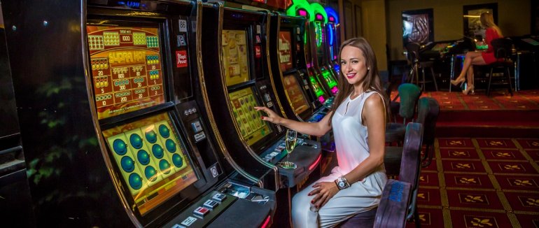 Симпатичная девушка улыбается, сидя за игровым автоматов в казино