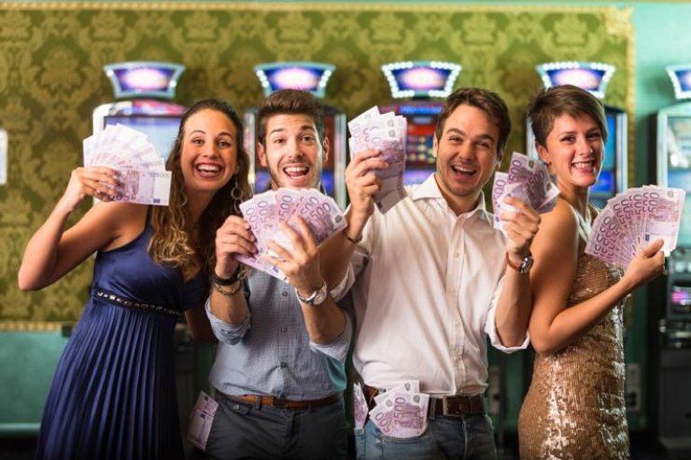 Радостные парни и девушки с денежными купюрами в руках в зале с игровыми автоматами