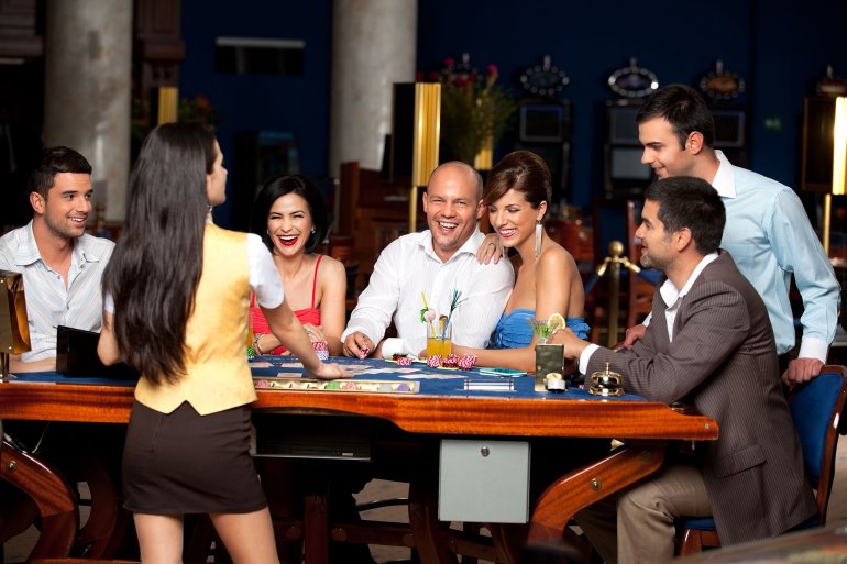Девушка крупье в короткой юбке ведет игру в блэкджек для молодой компании азартных игроков