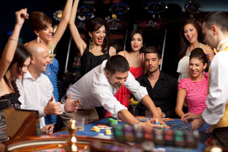 Зрители приветствуют игрока, сгребающего выигрыш, а его противник сидит с разбитым взглядом за столом для игры в рулетку