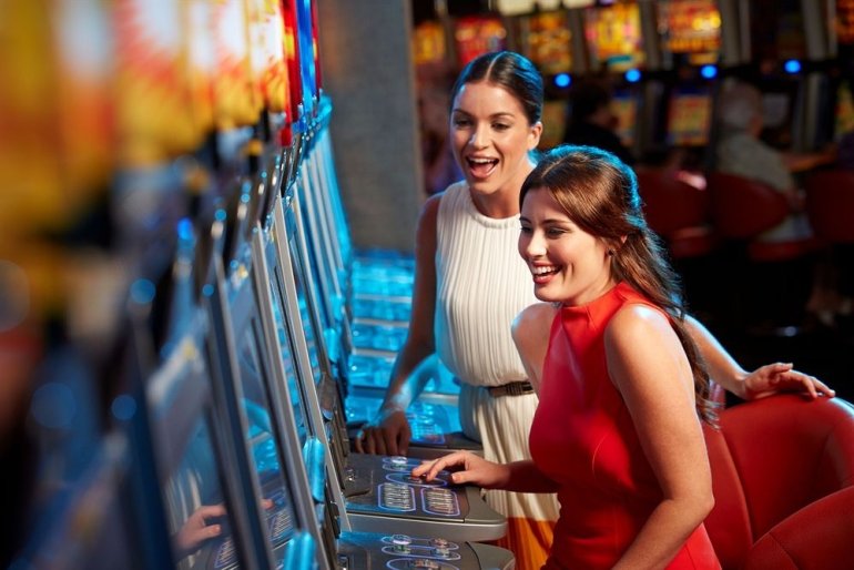 Две красивые девушки в нарядных платьях играют на игровых автоматах в престижном казино